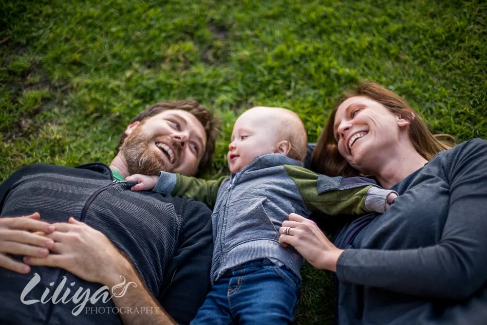 Parents and their baby lying in the grass, laughing