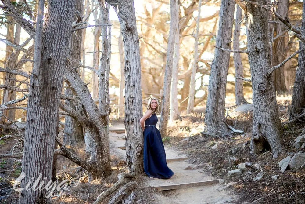 Woman in a navy gown on a path through cypress trees