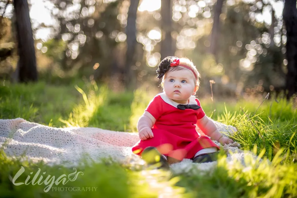 Baby girl in a red dress sitting in the grass