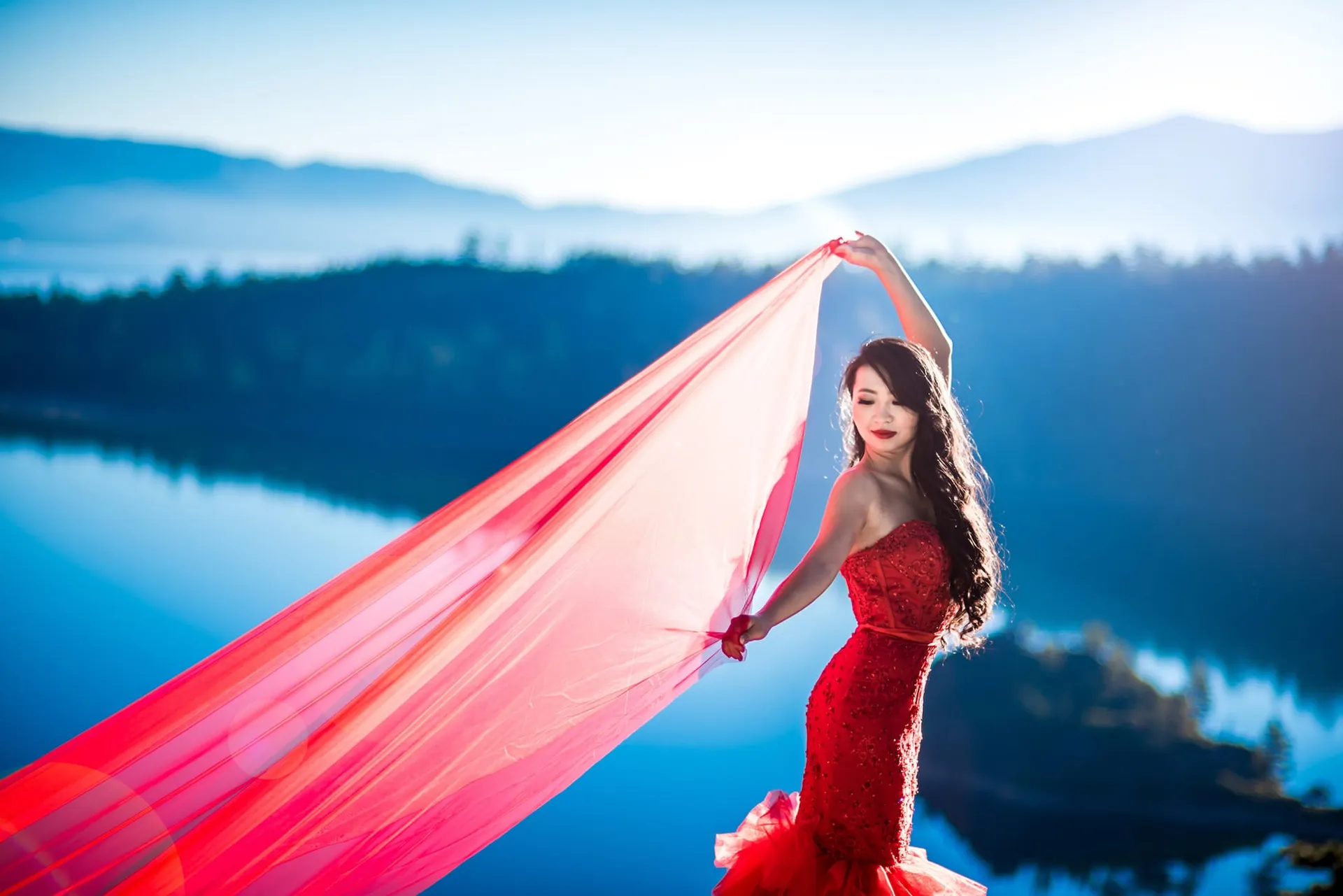 Woman in a red gown with flowing silk beside a mountain lake