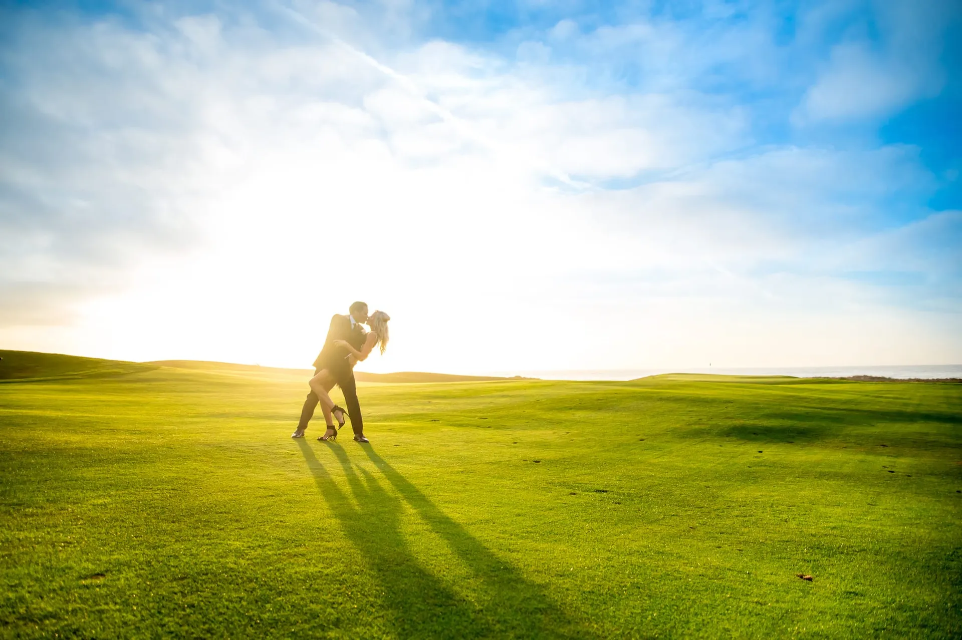 Couple silhouetted against the low sun on open grass